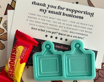 May include: Two turquoise blue silicone molds for making resin earrings. Each mold has a square shape with a small rectangular opening in the center. The molds are on a white surface with a floral pattern.