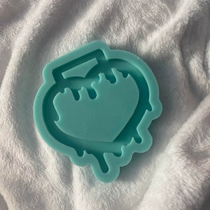 以下が含まれることがあります： 滴るハートの形をした薄い青色のシリコンモールド。モールドは、上部に小さなハンドルが付いたハートの隆起した輪郭を持っています。