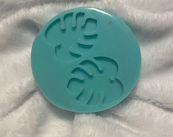 May include: A light blue silicone mold with two raised monstera leaf designs.