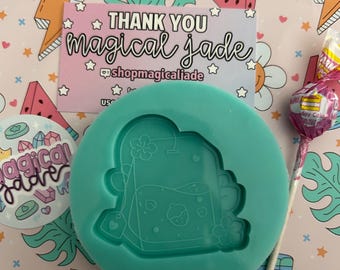 May include: A teal silicone mold shaped like a cartoon juice box with a flower and strawberry design. The mold is on a pink and white background with a pattern of watermelons, stars, and hearts. The text "THANK YOU magical jade" is on a pink and white card with a star pattern.