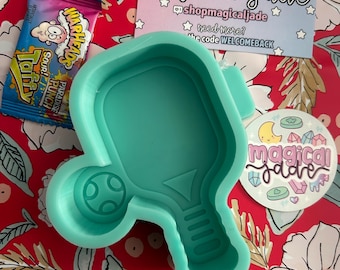 May include: A teal silicone mold in the shape of a pickleball paddle and ball, with a candy wrapper, a thank you card with text, and a sticker on a red floral background. The thank you card says "Thank You Magical Jade".