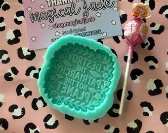 May include: A teal silicone mold with a floral border and the embossed text DESTROY THE PATRIARCHY NOT THE PLANET, accompanied by a pink Charms lollipop and a thank you card from magical jade with star icons and social media handles.