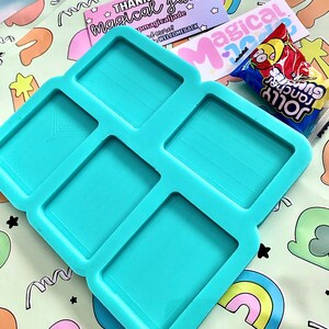May include: A turquoise silicone mould with six rectangular cavities. The mould is on a green and white background with a rainbow pattern. The text "Thank you magical jade" is visible on a pink and purple card.