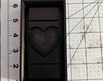 Op de afbeelding: Een donkerbruine chocolade reep met een hartvormig ontwerp. De chocolade reep zit in een rechthoekige vorm.