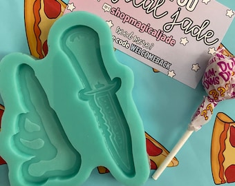 May include: A teal blue silicone mold with two shapes: a knife and a hand with a middle finger extended. The mold is on a blue background with pizza slices and a lollipop.