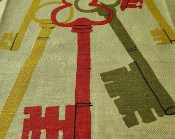 May include: A beige fabric with a repeating pattern of keys in red, yellow, and green. The keys are stylized and have a whimsical design. The fabric has a woven texture and the pattern is centered on the fabric. The fabric has the signature "Usma" in black with a copyright symbol.