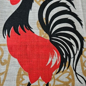 May include: A red rooster with a black head and tail feathers is depicted on a beige fabric background with a gold pattern. The rooster is standing on its two legs with its tail feathers fanned out behind it.