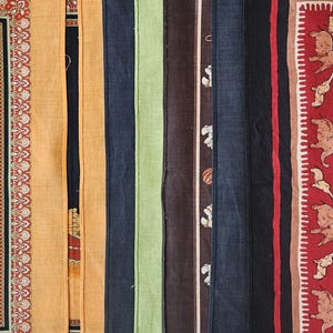 K&ouml;nnte beinhalten: Eine Sammlung farbenfroher Stoffbahnen mit jeweils einzigartigen Designs. Die Paneele umfassen Farbt&ouml;ne von Orange, Schwarz, Gr&uuml;n, Braun und Marineblau. Einige Paneele weisen gemusterte Bord&uuml;ren und dekorative Motive auf.