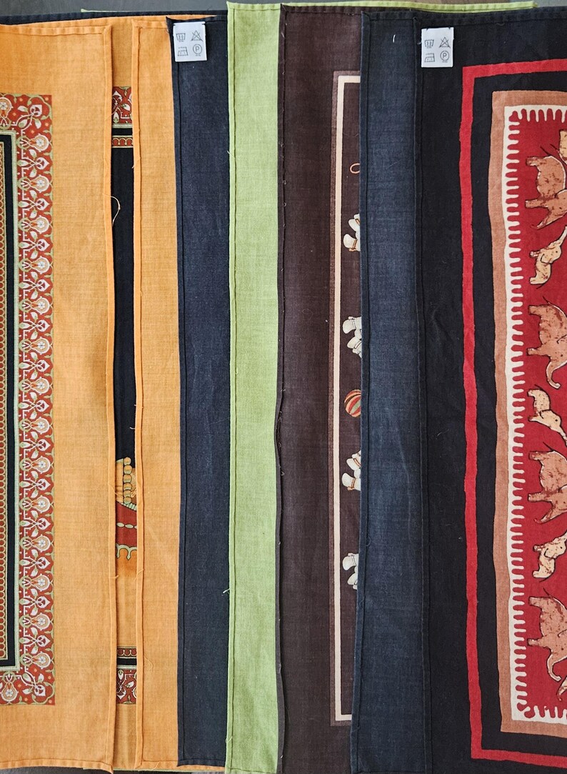 K&ouml;nnte beinhalten: Eine Sammlung farbenfroher Stoffbahnen mit jeweils einzigartigen Designs. Die Paneele umfassen Farbt&ouml;ne von Orange, Schwarz, Gr&uuml;n, Braun und Marineblau. Einige Paneele weisen gemusterte Bord&uuml;ren und dekorative Motive auf.