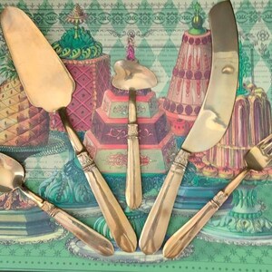 May include: Set of five gold-toned serving utensils, including a cake server, a butter knife, a spoon, a small heart-shaped server, and a fork. The utensils are arranged on a green and white patterned surface with images of cakes and pineapples.