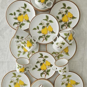 Puede incluir: Un juego vintage de porcelana con estampado de peras, con fondo blanco, ribete marrón y ramas de peral verdes con peras amarillas y flores blancas. El juego incluye tazas de té, platillos y platos de postre.