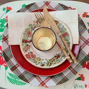 Könnte beinhalten: Ein Set aus drei roten und weißen karierten Tischsets mit weißem Hintergrund. Die Tischsets haben einen grün-weißen Rand. Ein weißer Teller mit rotem Rand liegt auf dem Tischset. Der Teller hat ein buntes Design mit Spielzeuglastwagen, einem Teddybär und anderen Kinderspielzeug. Eine goldene Metallschale liegt auf dem Teller. Zwei silberne Besteckteile liegen auf dem Teller. Eine weiße Serviette liegt auf dem Teller und dem Besteck.