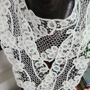 Op de afbeelding: Witte kantkraag met een delicaat bloemenpatroon. De kraag is gemaakt van een fijne, ingewikkelde kant en heeft een gegolfde rand.