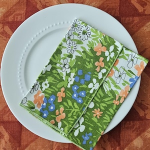 Puede incluir: Una servilleta de tela doblada con estampado floral verde, blanco y azul sobre un plato blanco.