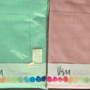 May include: Two packaged tablecloths, one green and one pink, with the brand name "Usna" and the text "Verve Table Top Coordinates". The green tablecloth is labelled "Seafoam" and measures 52 x 70 inches (132 x 178 cm). The pink tablecloth is labelled "Blush" and measures 52 x 70 inches (132 x 175 cm).