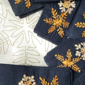 May include: A stack of dark blue fabric napkins with gold and white embroidered snowflake designs.
