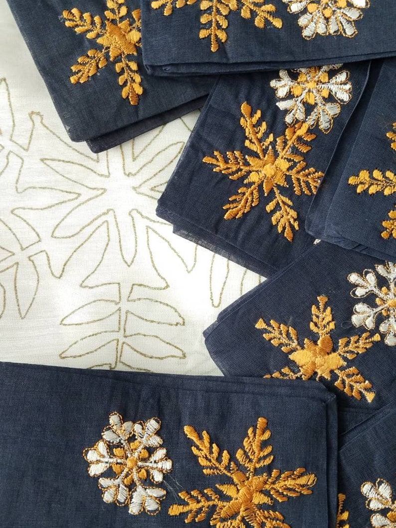 May include: A stack of dark blue fabric napkins with gold and white embroidered snowflake designs.