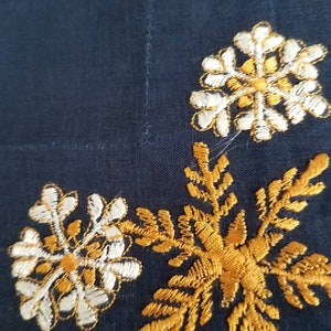 May include: A dark blue fabric with gold and white embroidered snowflakes. The snowflakes are in a corner of the fabric.