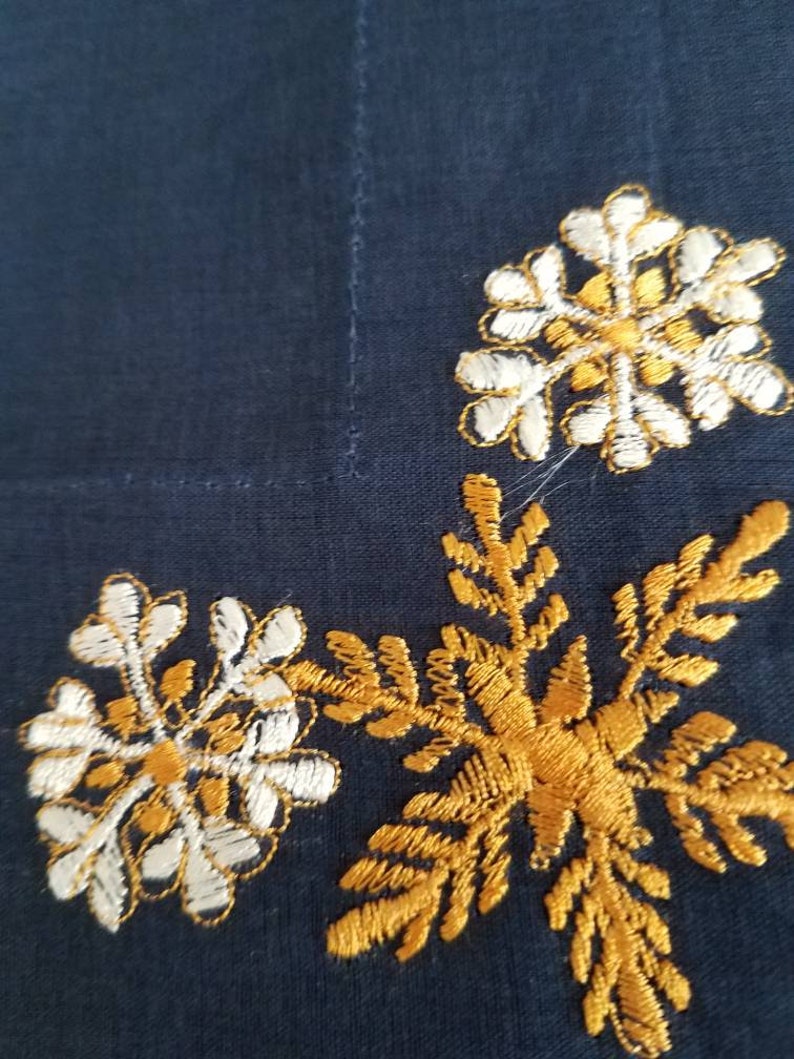 May include: A dark blue fabric with gold and white embroidered snowflakes. The snowflakes are in a corner of the fabric.