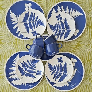 May include: Set of six blue and white ceramic plates featuring a fern leaf design. The plates are arranged in a circle with four smaller plates inside two larger plates. The plates have the word "Usna" written on the bottom.