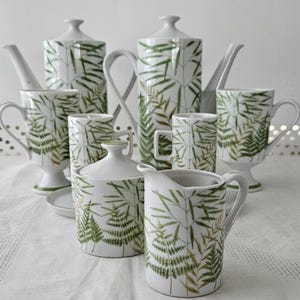 May include: A white porcelain tea set with a fern leaf pattern. The set includes a teapot, creamer, sugar bowl, and four cups.