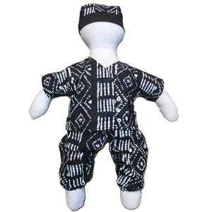 May include: A doll wearing a black and white patterned short-sleeved shirt, matching pants, and a small black and white cap. The fabric features a geometric print with white lines and diamond shapes on a black background. The doll has a plain white body.