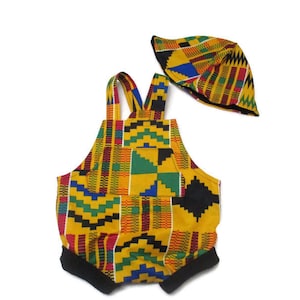May include: A yellow, green, red, and black patterned romper with matching hat. The romper has a bib style top and black straps. The hat is a bucket style.