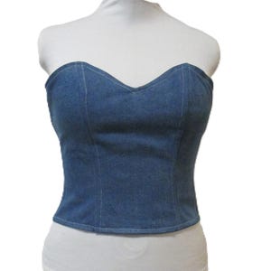 May include: A strapless denim corset top. The blue top has a sweetheart neckline and is displayed on a white mannequin. The corset is made of denim material and has visible stitching details.