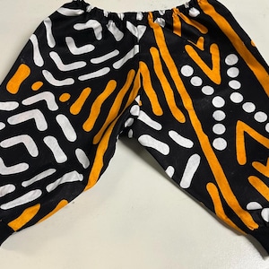 May include: Black pants with a white and orange geometric pattern. The pants have a drawstring waistband and elastic cuffs.