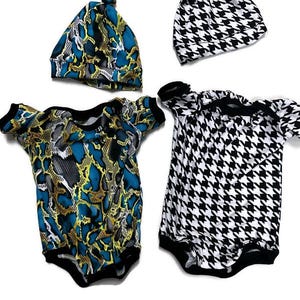 May include: Two baby onesies and two matching hats. One onesie and hat are black and white with a houndstooth pattern. The other onesie and hat are blue, yellow, and white with a snake skin pattern.