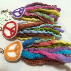 Pode incluir: Três chaveiros coloridos com o símbolo da paz com um fecho de metal. Cada chaveiro tem um símbolo da paz de cor diferente e um longo tassel de fio colorido.