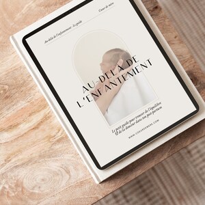 Peut inclure: Une tablette numérique blanche avec un cadre noir affichant un guide intitulé "Au-delà de l'enfantement - Le guide" avec une photo d'un bébé tenu par une main. Le texte sur la tablette indique "Coeur de mère", "AU-DELA DE L'ENFANTEMENT", "Le petit guide pour trouver de l'équilibre & de la douceur dans ton post-partum", et "www.COEURDEMERE.COM".