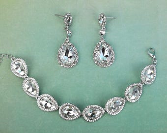 May include: A matching jewelry set featuring a bracelet and earrings. The bracelet and earrings have a silver-tone metal setting with clear, teardrop-shaped rhinestones. The earrings are dangling, and the bracelet has an adjustable chain.