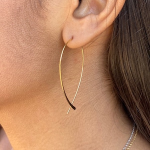 May include: Gold hoop earrings with a unique curved design. The earrings are thin and delicate, and they hang from the earlobe.