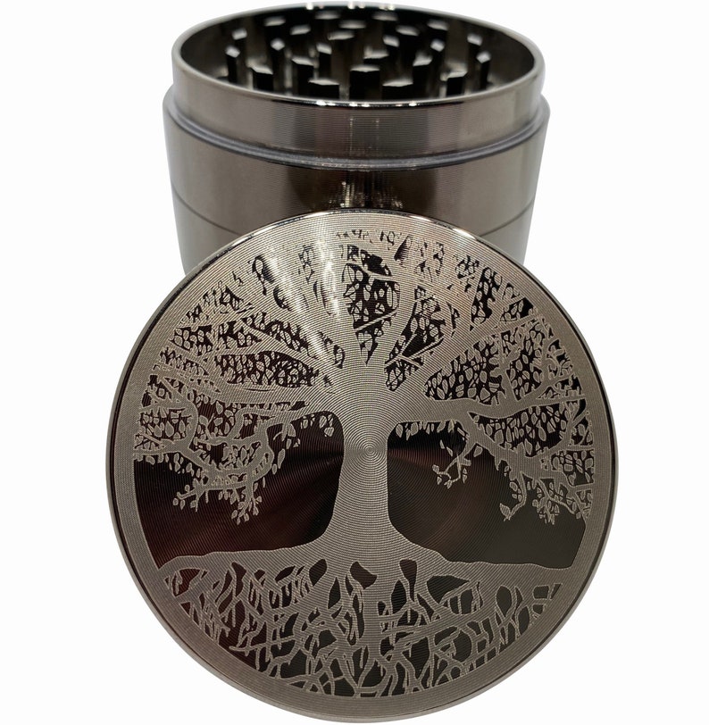Op de afbeelding: Een zilveren metalen grinder met een levensboomontwerp op de deksel. De grinder heeft een ontwerp met vier delen en een compartiment voor het bewaren van kruiden.
