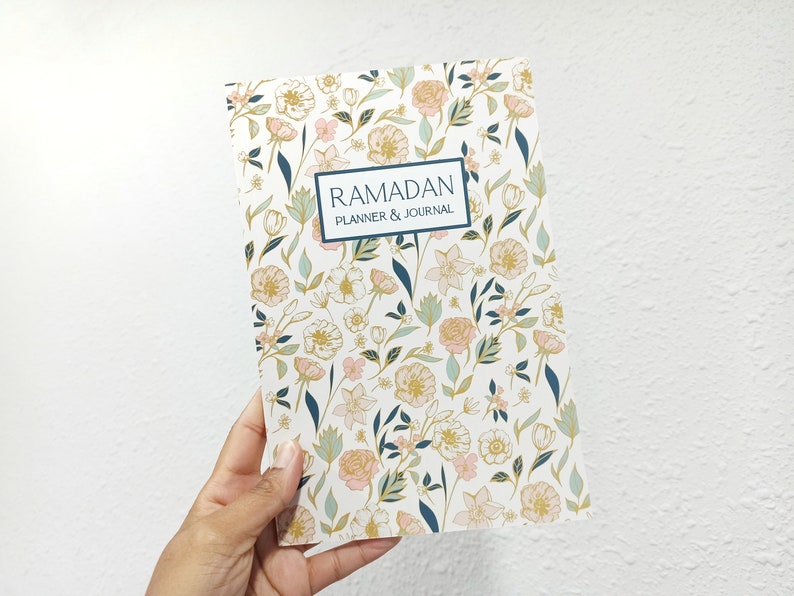 A hand holding a white journal with a floral pattern on it