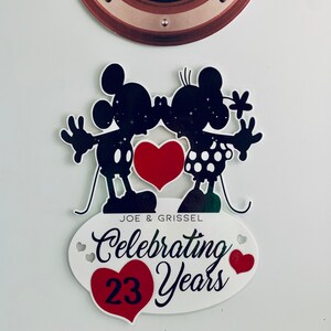 Może przedstawiać: Czarna sylwetka Myszki Miki i Minnie Mouse całujących się z czerwonym sercem w środku. Poniżej znajduje się owal z tekstem "JOE & GRISSEL Celebrating 23 Years" z czerwonym sercem po obu stronach tekstu.