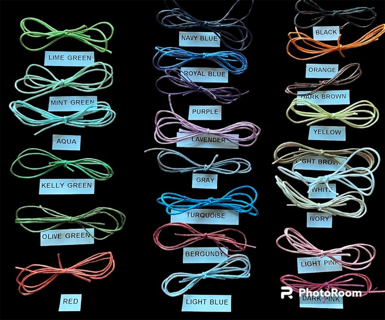 May include: A collection of shoelaces in various colors, including lime green, navy blue, and red, are displayed against a black background. Each pair is neatly tied into a bow, with labels indicating the color name. Colors include black, orange, and dark pink.