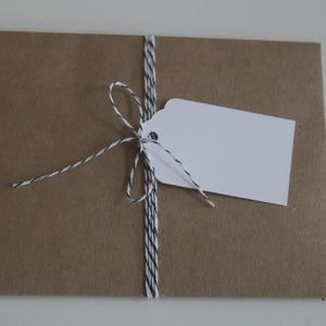 May include: A brown paper package tied with black and white twine. A white tag is attached to the twine. The package is on a white surface. The package is likely for a gift or a product.