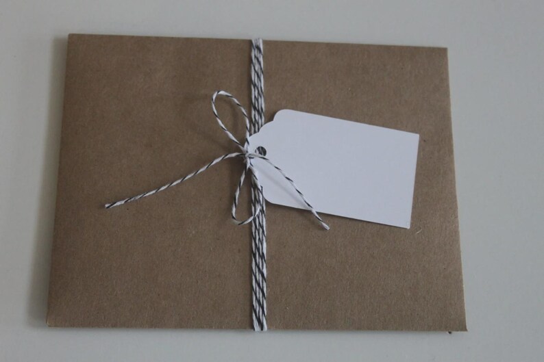 May include: A brown paper package tied with black and white twine. A white tag is attached to the twine. The package is on a white surface. The package is likely for a gift or a product.