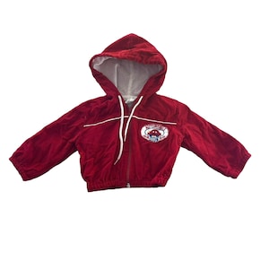 Puede incluir: Chaqueta roja con capucha, cremallera blanca y ribetes blancos. La chaqueta tiene un parche en la parte delantera que dice "Automobile Club" con un gráfico de un coche rojo.