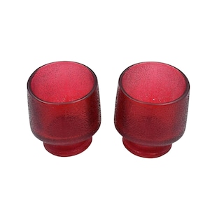 Könnte beinhalten: Zwei rote Glas-Schnapsgläser mit strukturierter Oberfläche.