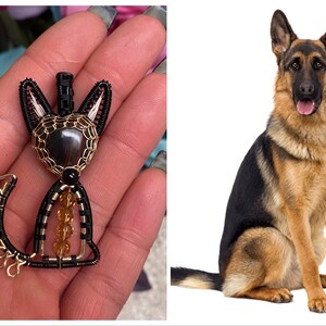 May include: A black and gold wire-wrapped cat figurine with a brown gemstone eye. The figurine is sitting on a hand.