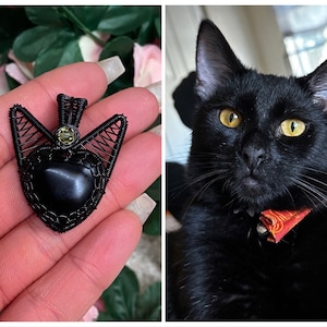 Könnte beinhalten: Ein schwarzer, drahtgewickelter Anhänger mit einem schwarzen herzförmigen Stein und einem kleinen grünen Edelstein. Der Anhänger wird in einer Hand gehalten.