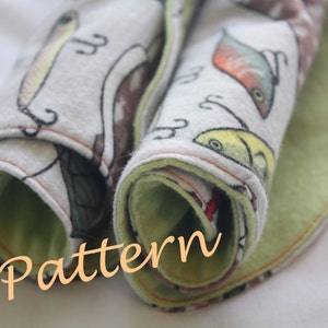 May include: A rolled up fabric with a green and white fish print. The fabric is folded over and has a green border. The text "E Pattern" is written in orange on the fabric.