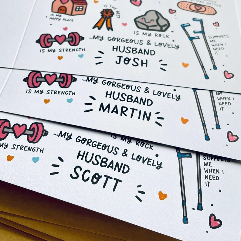 May include: Three white greeting cards featuring colorful hand-drawn illustrations of a pink barbell, a grey rock, and blue crutches. Text includes "IS MY STRENGTH", "IS MY ROCK", "SUPPORTS ME WHEN I NEED IT", and "MY GORGEOUS & LOVELY HUSBAND" with names JOSH, MARTIN, and SCOTT.