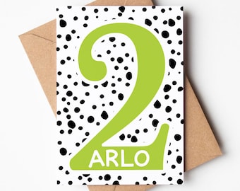 Puede incluir: Una tarjeta blanca con un patrón de lunares negros y blancos. Un gran número dos verde con el nombre "ARLO" dentro del número.