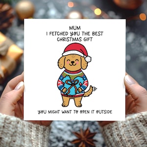 May include: A square greeting card featuring a cartoon golden dog wearing a red Santa hat and a patterned sweater, holding a blue gift. The text reads: MUM I FETCHED YOU THE BEST CHRISTMAS GIFT YOU MIGHT WANT TO OPEN IT OUTSIDE.