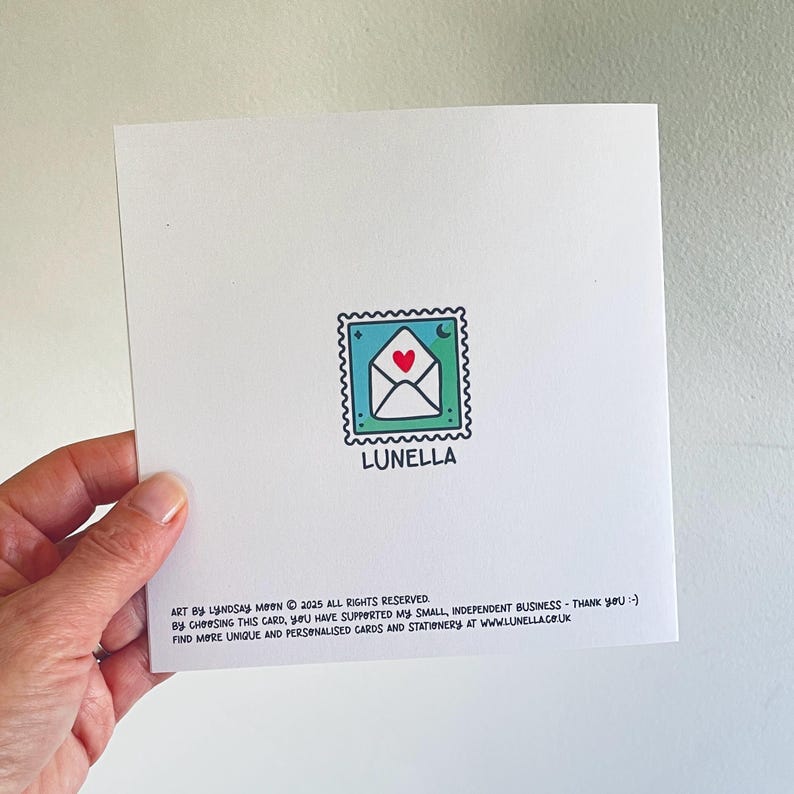 May include: Square white card with a stamp-like illustration of an envelope with a heart and moon. The word "LUNELLA" is below the stamp. Text at the bottom reads "ART BY LYNDSAY MOON &copy; 2025 ALL RIGHTS RESERVED..." and a website address.