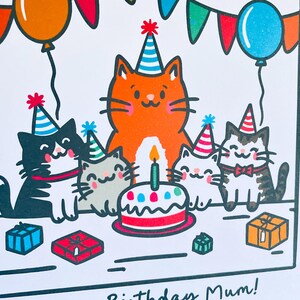 May include: A birthday card featuring cartoon cats wearing party hats, gathered around a cake with a lit candle. Balloons and presents are also shown. The card has the text "Birthday Mum!"
